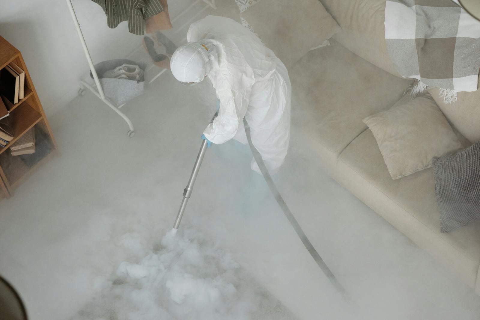 Person in White Protective Clothing Fumigating a Rug in a Living Space